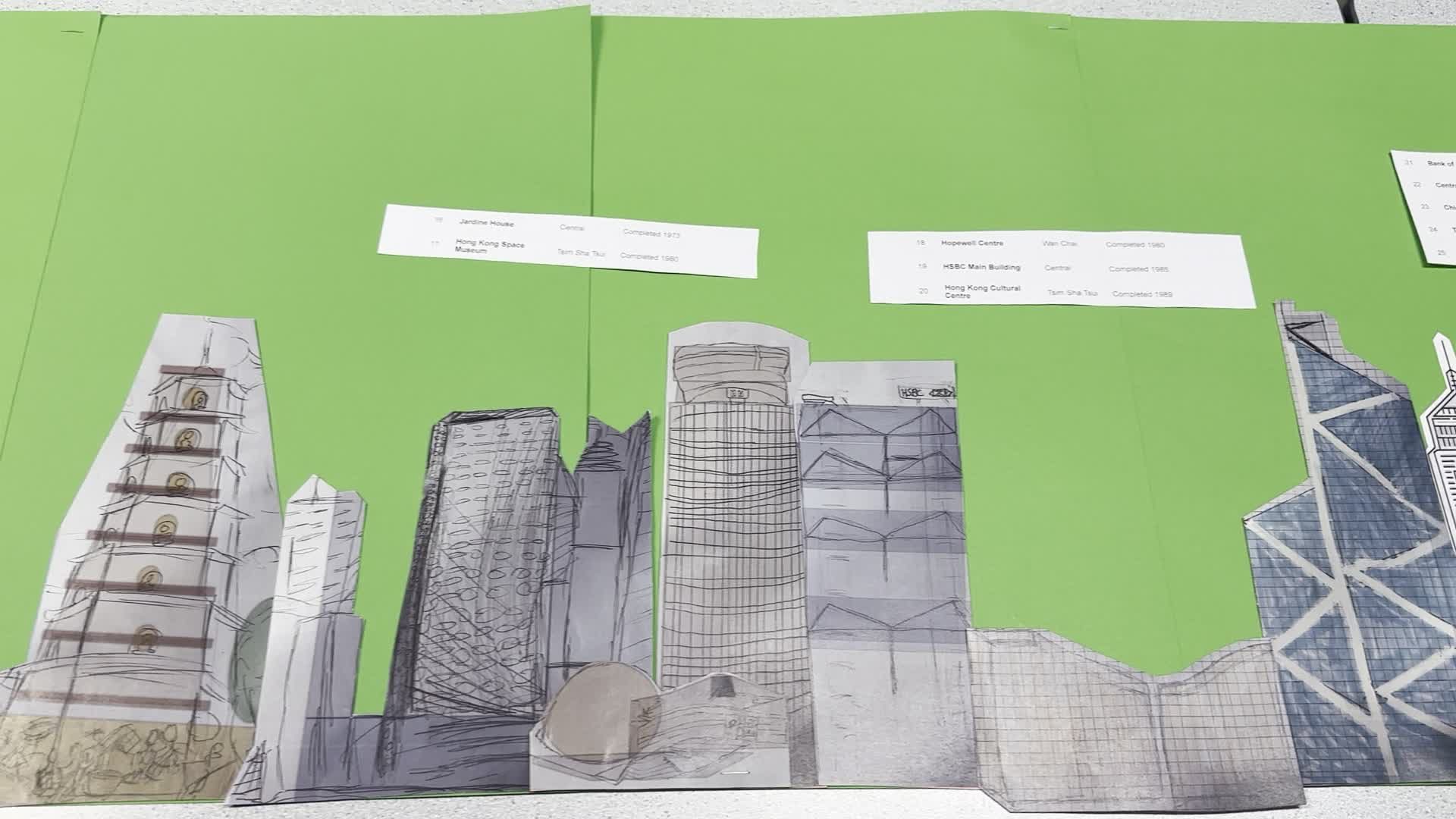Coloured paper cut-outs of Hong Kong buildings standing in a row on green card