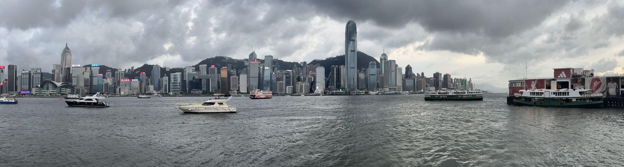 Panoramic photo of the Hong Kong Island skyline across Victoria Harbour under grey clouds